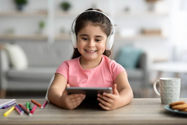 Menina bonito vestindo fones de ouvido sem fio relaxante com tablet digital em casa — Fotografia de Stock