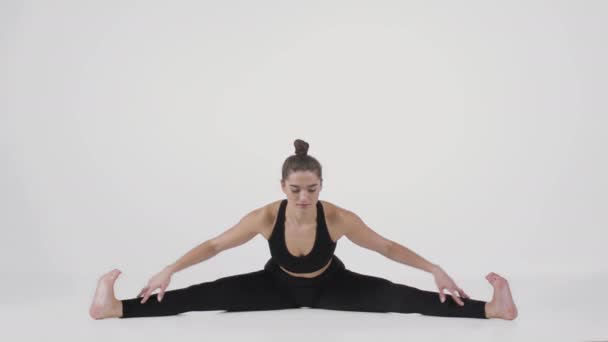 Ung flexibel dam sitter på golvet med benen brett isär och lutar sig framåt, öva Upavistha Konasana position — Stockvideo
