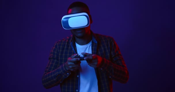 Hazard VR. Młody czarny facet gra w gry wideo z joystickiem i wirtualnej rzeczywistości zestaw słuchawkowy, neon światła tła — Wideo stockowe