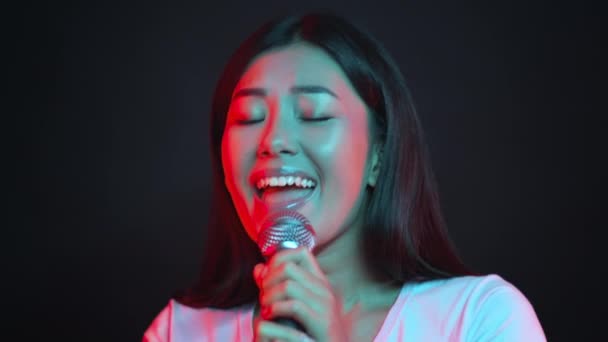 Крупный план портрета профессиональной азиатской певицы, выступающей на сцене, поющей в микрофон и улыбающейся в камеру — стоковое видео