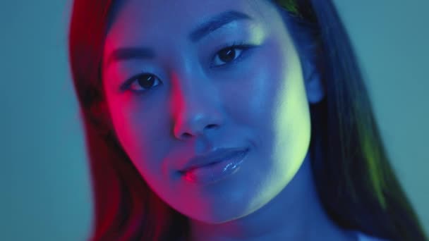 Крупный студийный портрет молодой модной счастливой азиатки, позирующей и улыбающейся перед камерой в красном и синем неоновом свете — стоковое видео