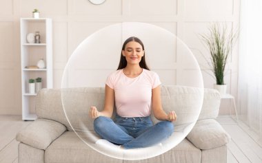 Sakin, mutlu, gülümseyen, Avrupalı bir kadın oturma odasındaki kanepede meditasyon yapıyor.