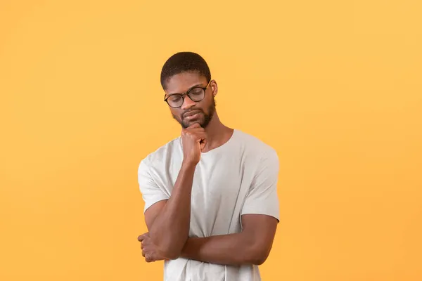 Pensativo afroamericano chico tocando la barbilla y pensando en algo, de pie sobre el fondo amarillo — Foto de Stock