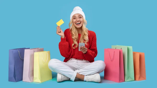 Senhora sorridente com sacos de compras usando celular e cartão de plástico — Fotografia de Stock