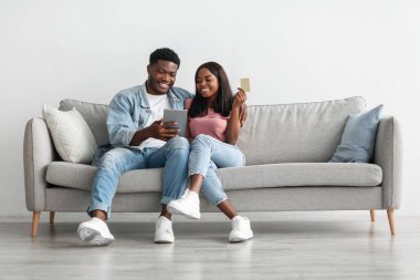 Siyah çift evde tablet ve kredi kartı kullanıyor.