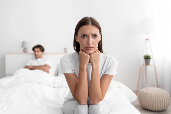 Ongelukkig beledigd europees jong vrouw zitten op bed weg te keren van echtgenoot, negeren hem in witte slaapkamer — Stockfoto