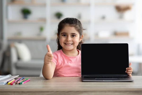 Menina pequena feliz que mostra o portátil com tela preta e polegar de Gesturing acima — Fotografia de Stock