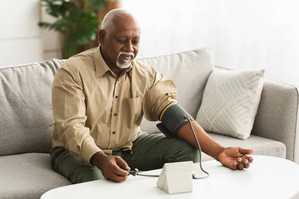 Зрелый африканский человек измеряет артериальное давление с помощью медицинского устройства в помещении — стоковое фото