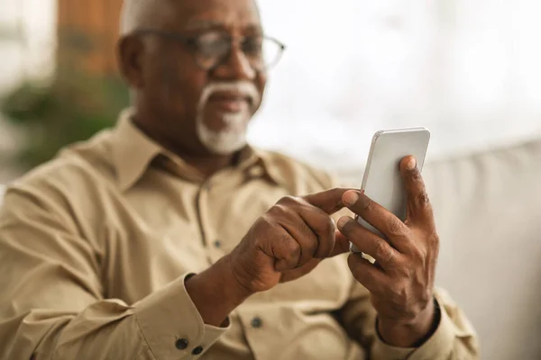 ソファの屋内に座っているスマートフォンのテキストを使用してシニアアフリカ人男性 — ストック写真