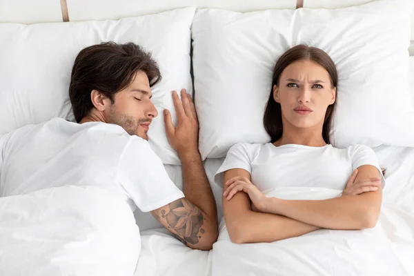 Boos ongelukkige blanke duizendjarige vrouw wakker met gekruiste armen in bed met slapende man in slecht — Stockfoto