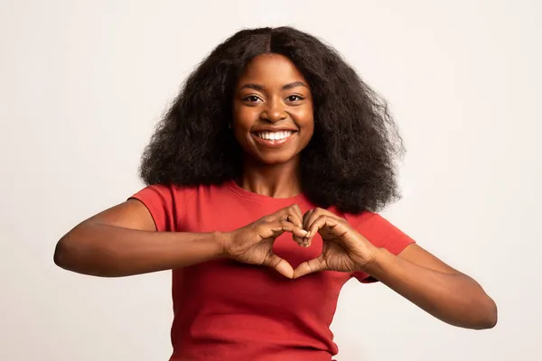 Glimlachende jonge Afro-Amerikaanse dame tonen hart gebaar met handen in de buurt van de borst — Stockfoto