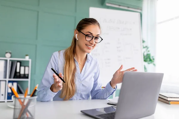 E-lärande. Kvinnlig lärare som har videosamtal med elever och klassgrupp, använder bärbar dator och bär trådlösa hörlurar — Stockfoto