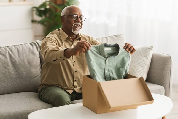 Homme noir senior déballage boîte regardant chemise à la maison — Photo