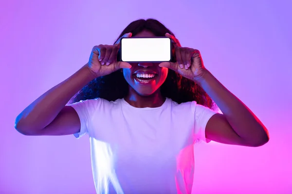 Smartphone scherm mockup. Zwarte vrouw bedekt ogen met lege telefoon, biedt ruimte voor mobiele app in neon licht — Stockfoto