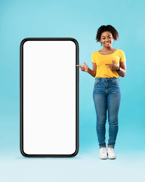 Siyah kadın cep telefonunu işaret ediyor. Mobil uygulama için boş yeri var, mavi arka plan. Akıllı telefon ekran modeli — Stok fotoğraf