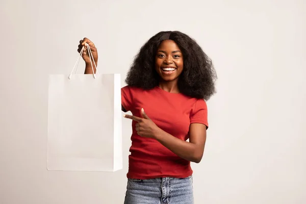 Glückliche schwarze Frau zeigt auf leere Einkaufstasche mit Kopierraum — Stockfoto