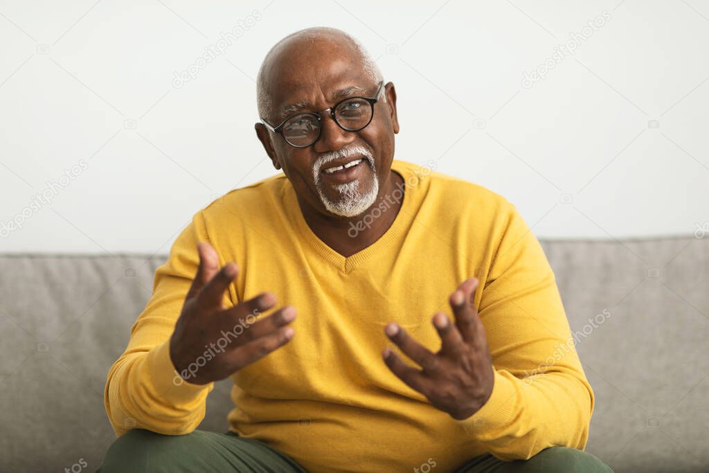 Senior African Man Talking To Camera Sitting On Couch Indoors