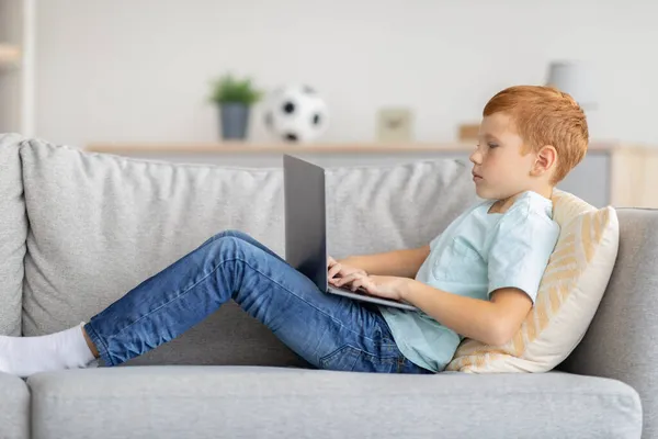 Redhead chlapec pomocí notebooku, hraní online videohry, boční pohled — Stock fotografie