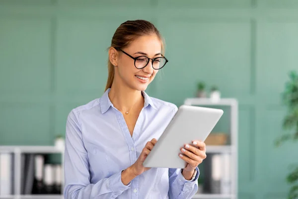 Mutlu iş kadını ofis içindeki iş yerinde dijital tablet kullanıyor, belgeleri internetten okuyor, e-postaları kontrol ediyor. — Stok fotoğraf