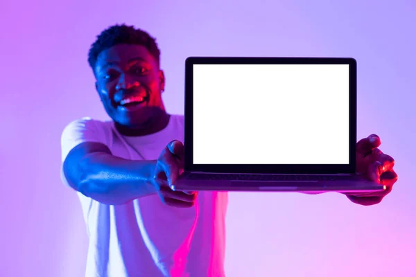 Fröhlicher schwarzer Kerl mit Laptop-PC und leerem weißen Bildschirm mit Platz für Attrappen, Werbung für neue Website im Neonlicht — Stockfoto