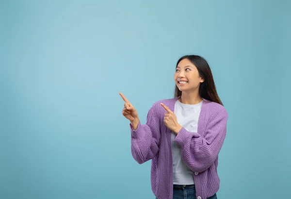 Havalı Asyalı kadın mavi stüdyo arka planında boş alana bakıp heyecan verici mesajlar veya reklamlar gösteriyor. — Stok fotoğraf