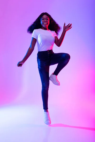 Aktif, enerjik genç siyahi bir kadının neon ışıkta zıplamasının tam boy portresi. — Stok fotoğraf