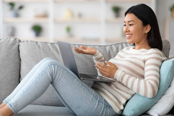 Positivo giovane asiatica femmina utilizzando il computer portatile per videochiamata a casa — Foto Stock