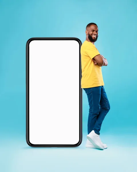 뜨거운 제안, 온라인 판매. 펑키 흑인젊은 남자가 파란 배경 위에 흉내를 내며 큰 핸드폰 근처에 서 있습니다 — 스톡 사진