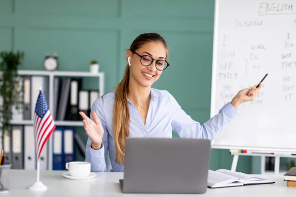 Happy young teacher conducting English lesson on web, using laptop, explaining grammar rules from office interior — Stock Photo, Image