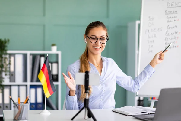 Online talenschool. Vriendelijke vrouwelijke leraar geeft Duitse les, met behulp van smartphone, uitleggen grammatica — Stockfoto