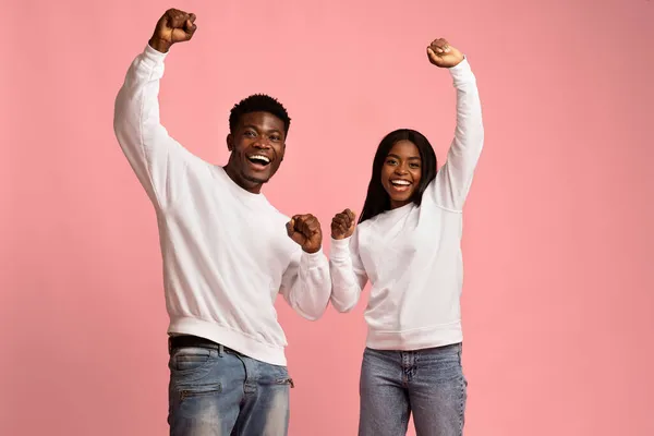 Cheery black couple celebrating success on pink studio background — Stock Photo, Image