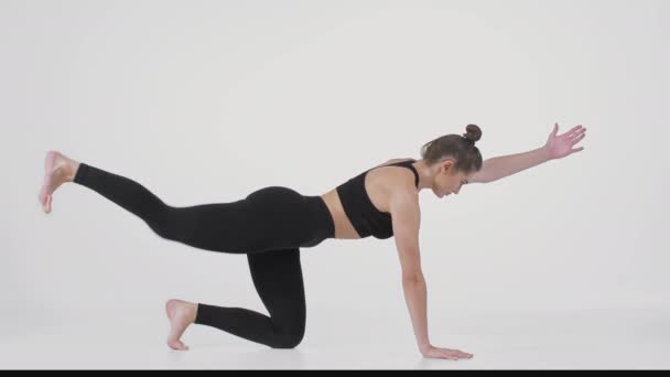 Ung sportig kvinna knäböjer på golvet och tränar rygg stretching pose, höja ben och hand och curling kropp — Stockvideo