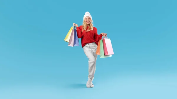 Mulher sorridente no chapéu de inverno segurando sacos de compras no estúdio — Fotografia de Stock