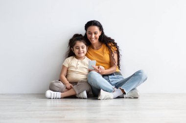 Mutlu Orta Doğulu anne ve küçük kızı evde akıllı telefonla dinleniyor.