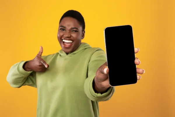 과도 한 체중을 가진 아프리카 여성, 노란 배경 위에 빈 핸드폰 화면을 보여 주다 — 스톡 사진