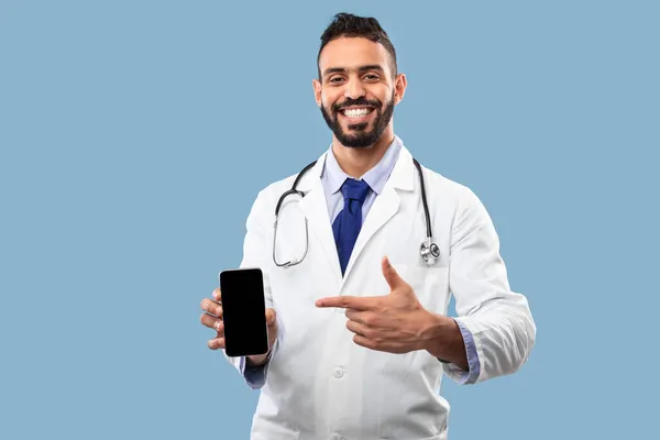 Terapeuta árabe homem mostrando telefone com tela em branco, fundo azul — Fotografia de Stock