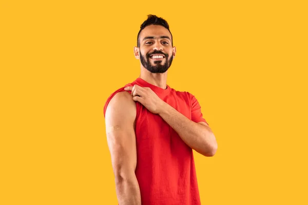 Felice vaccinato arabo maschio mostrando braccio dopo la vaccinazione, sfondo giallo — Foto Stock