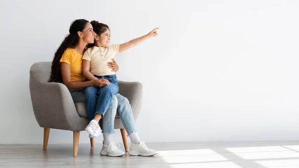 Mamá y su hijo femenino señalando a un lado mientras se relaja en el sillón en casa —  Fotos de Stock