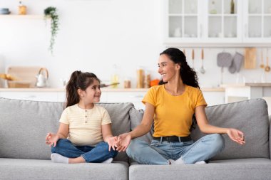 Sevimli küçük kız ve genç annesi evde birlikte meditasyon yapıyorlar.