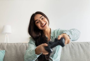 Joystickli neşeli Hintli kadın çevrimiçi video oyunları oynuyor, oturma odasında eğleniyor.