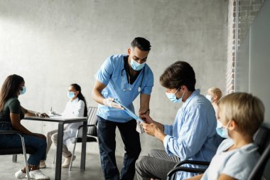 Aşılanmadan önce çok ırklı hastaların tıbbi tabloları doldurmasına yardım eden Arap doktor