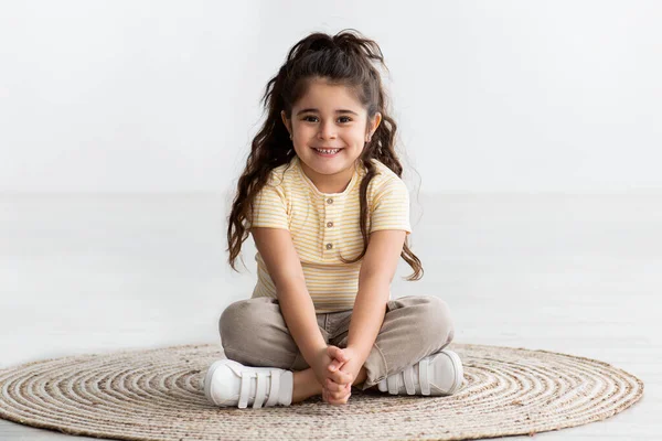 Retrato de linda niña sonriente sentada en la alfombra de mimbre en casa, — Foto de Stock