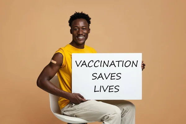 Afro-americano chico publicidad vacunación, celebración motivacional placa y sonriendo en cámara —  Fotos de Stock
