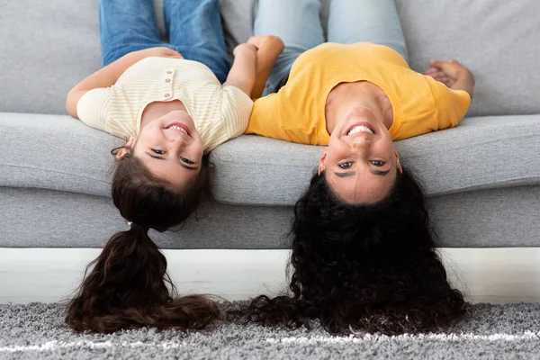 Glad rolig rolig ung mor och liten dotter ligger på soffan upp och ner — Stockfoto
