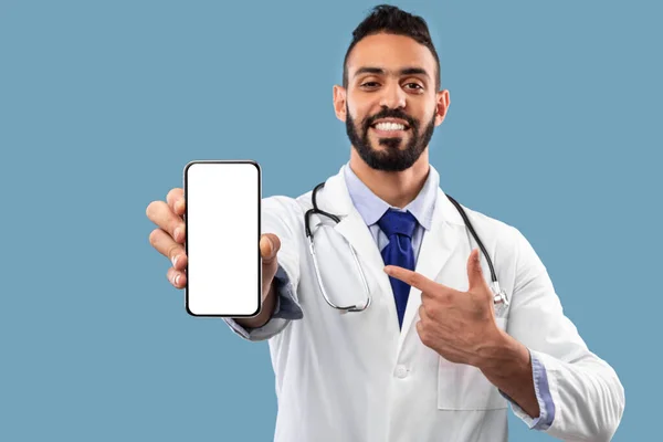 Médico masculino de Oriente Medio que muestra la pantalla vacía del teléfono celular sobre fondo azul — Foto de Stock