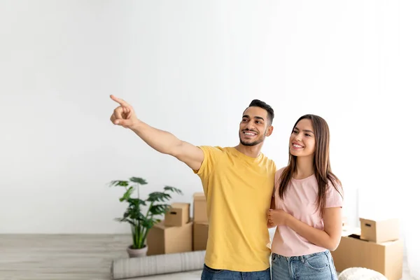 Alegre joven pareja multirracial en su casa entre cajas de cartón en el día de la mudanza, pensando en la colocación de muebles —  Fotos de Stock