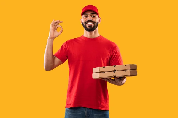 Nahost-Kurier Guy hält Pizzaschachteln und gestikuliert Okay, gelber Hintergrund — Stockfoto