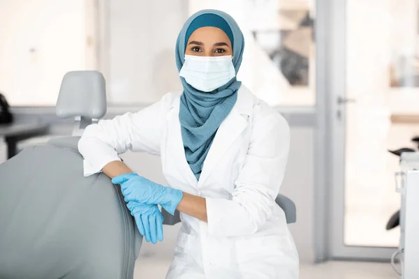Profissional muçulmano dentista feminino vestindo máscara facial e hijab posando no local de trabalho — Fotografia de Stock