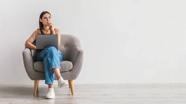 Mulher millennial pensativo com laptop pc sentado em poltrona, olhando para o espaço vazio contra a parede branca, banner — Fotografia de Stock