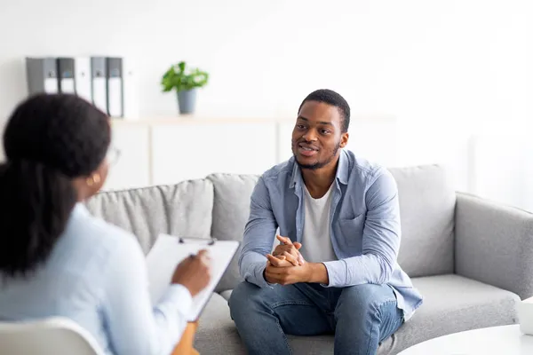 Hatékony pszichoterápia. Fiatal fekete fickó pszichológussal beszélget, szakmai segítséget kap a mentális egészségügyi klinikán. — Stock Fotó